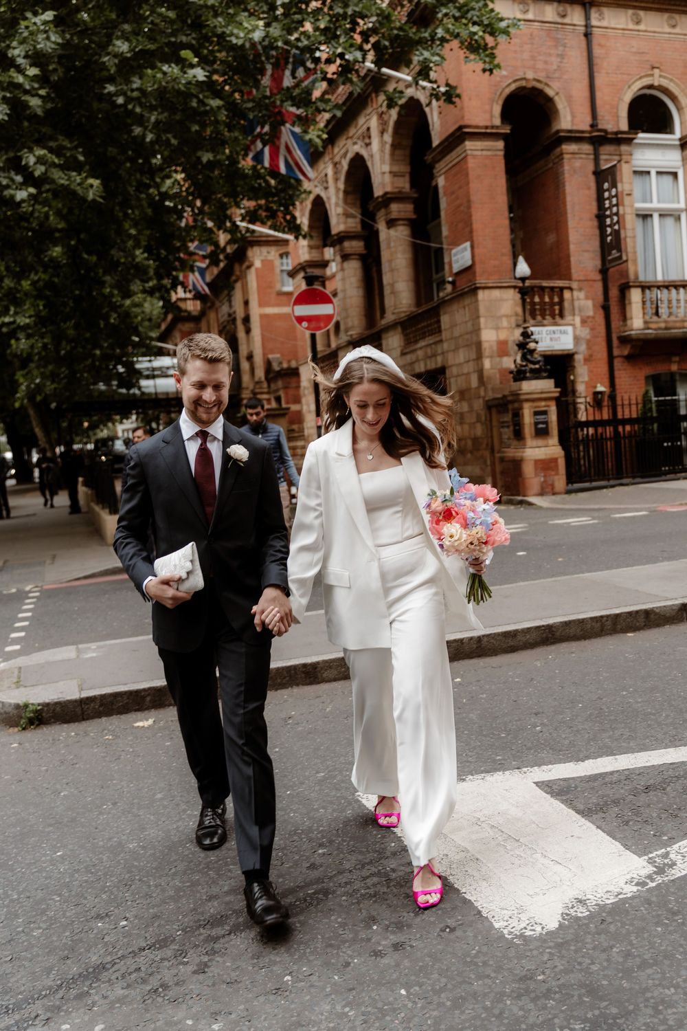 A wedding couple walks together on a city street with historic brick buildings in the background.
