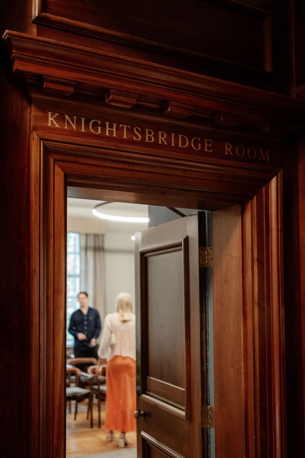 Wooden doorway entrance to the Knightsbridge Room with elegant carved lettering above the dark mahogany door frame.
