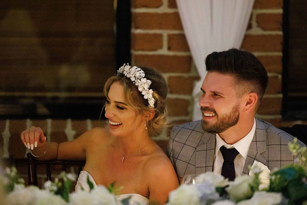 Bride and groom share a happy moment seated at their wedding reception table with floral arrangements.