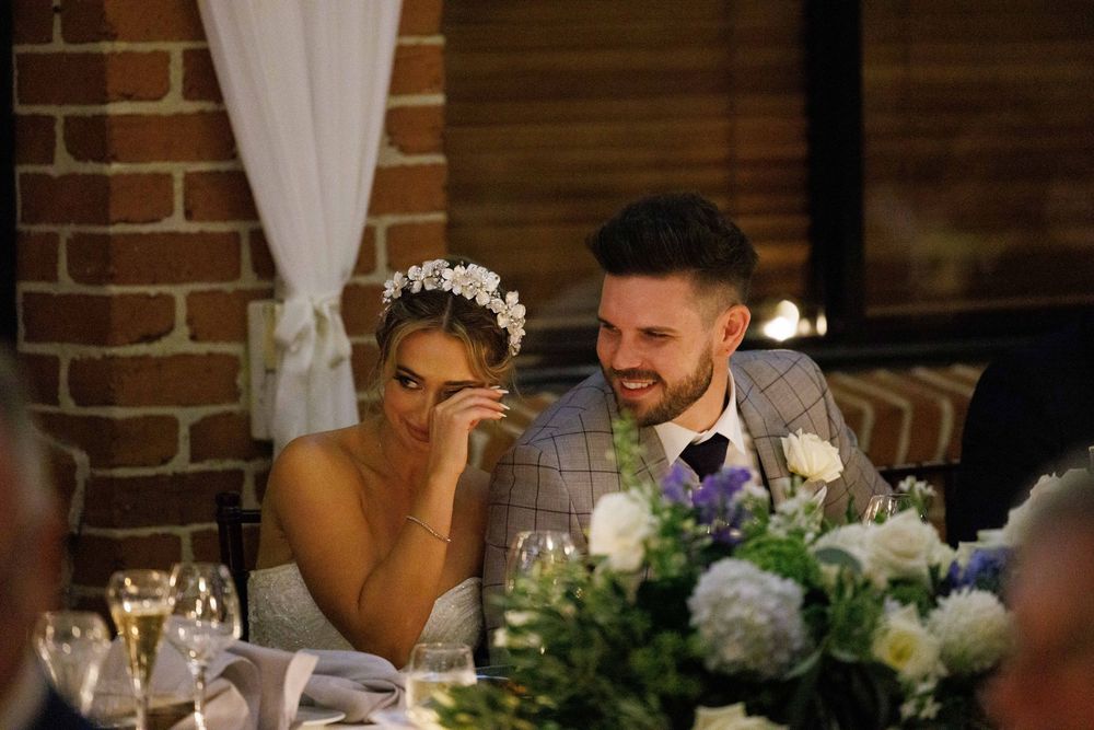 Bride and groom laugh together at wedding reception table with floral centerpieces.