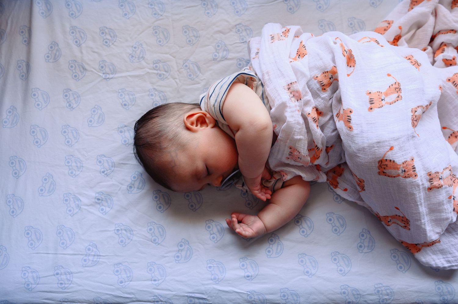 A newborn baby wearing a white and orange floral outfit lies on a soft gray blanket.