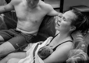 Fresh newborn baby wrapped in blanket held by its mother moments after birth