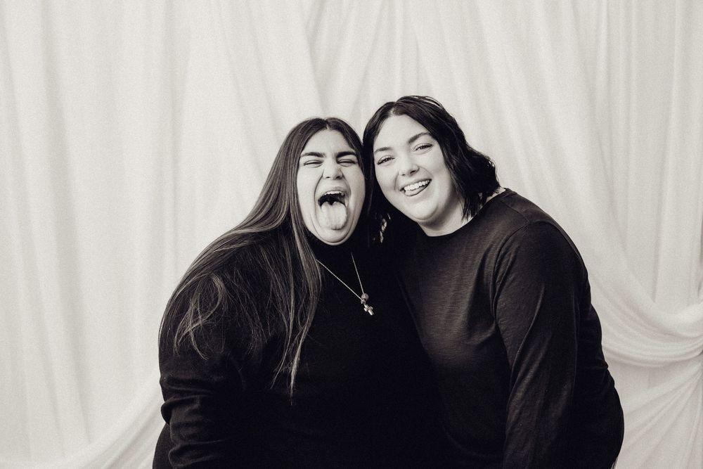Two women laughing and making silly faces in a fun black and white studio portrait.
