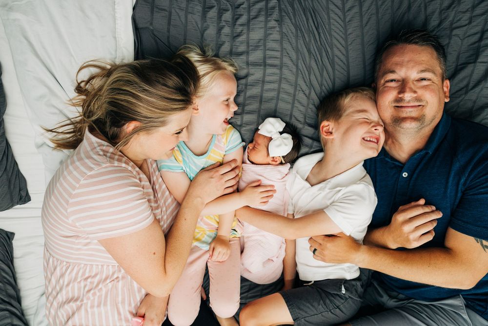 Family laughs together while laying on gray blanket during casual lifestyle Charlotte newborn photo session.