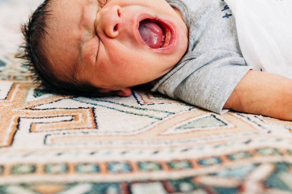 Baby lying on patterned blanket yawns widely during Charlotte newborn photography