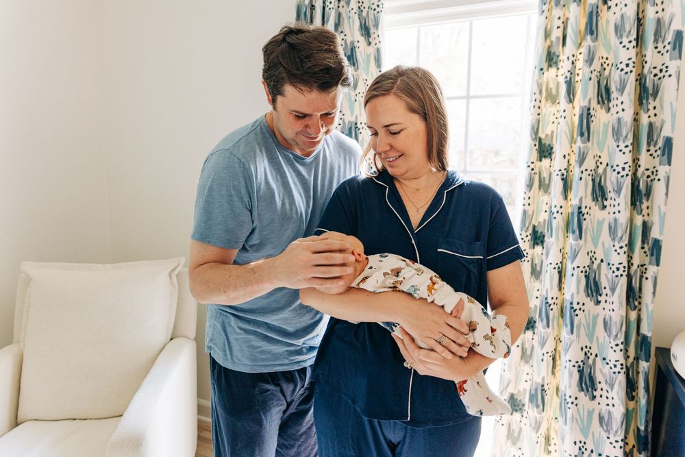 A couple shares an intimate moment while holding their newborn baby in a bright, modern living room.