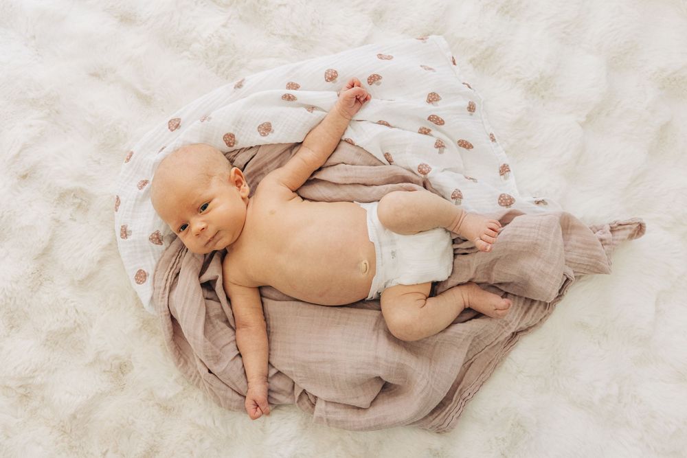 A newborn baby lies on soft beige bedding in a series of peaceful resting poses.