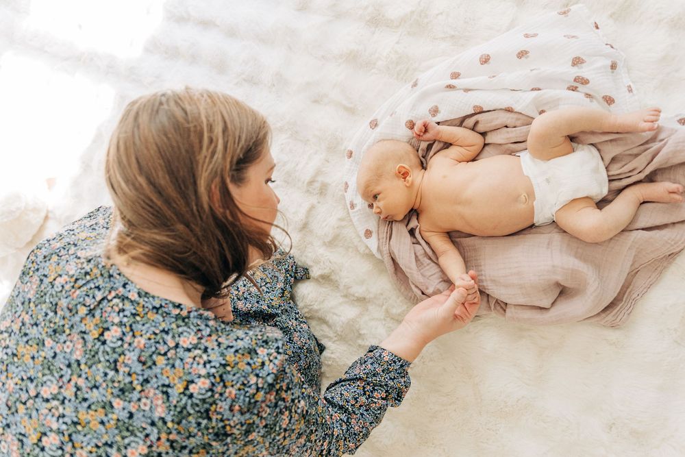 A tender moment captured between a parent and baby lying together on a soft white blanket.