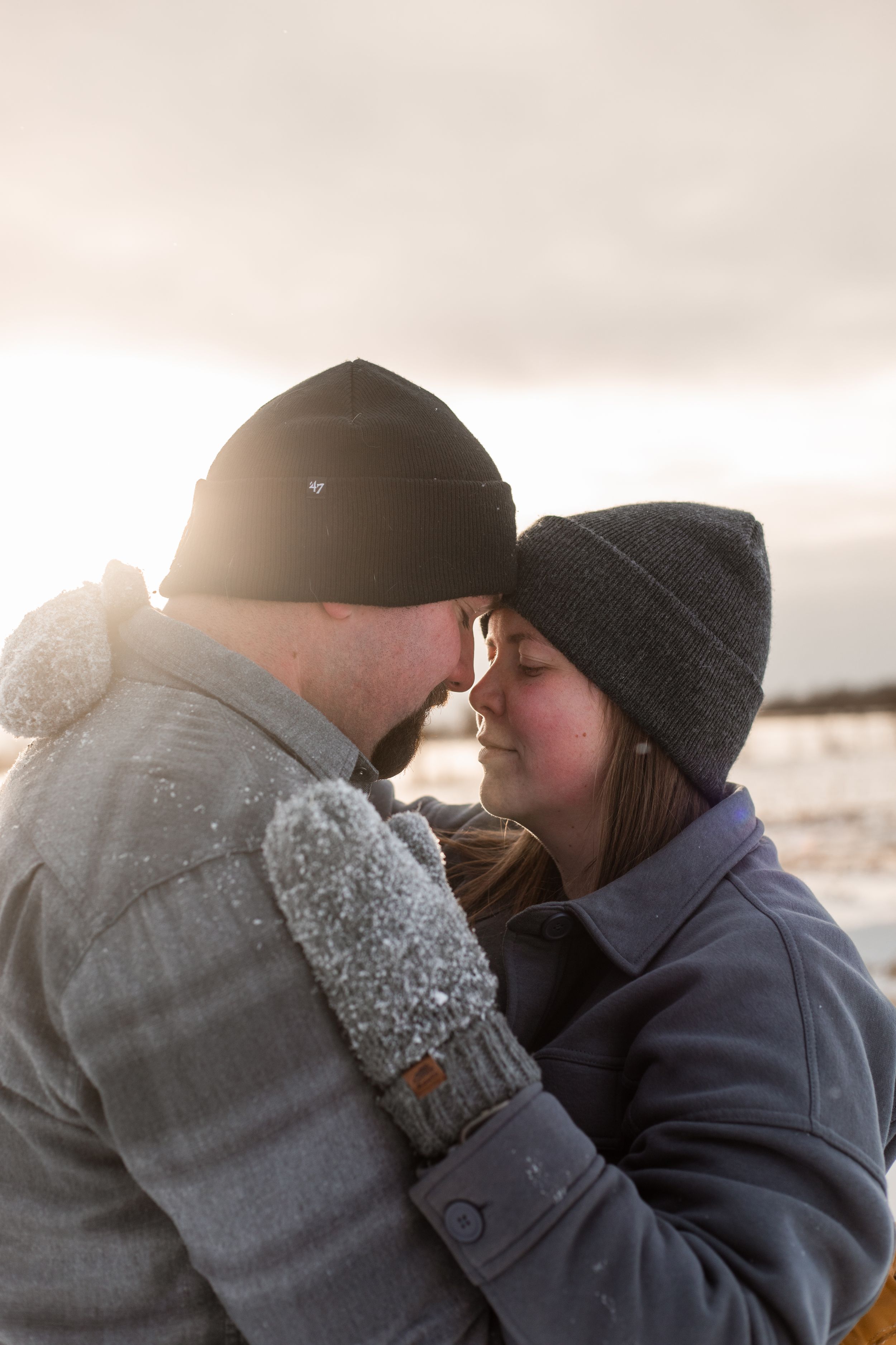 A couple in winter clothing sharing an intimate moment against a cloudy sky backdrop.