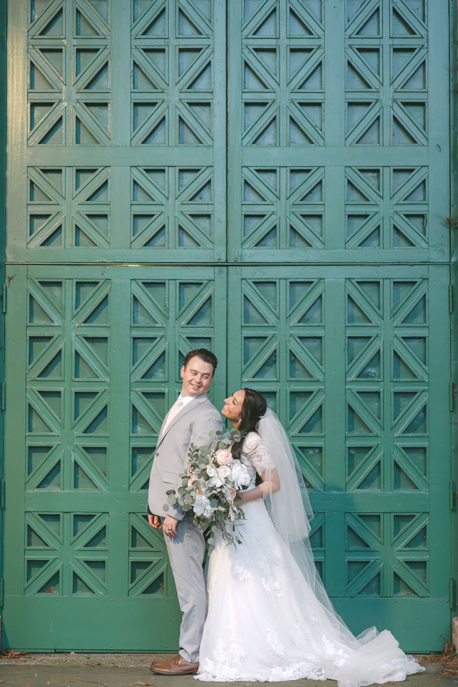 Wedding couple poses playfully against a backdrop of geometric turquoise doors at an outdoor venue.