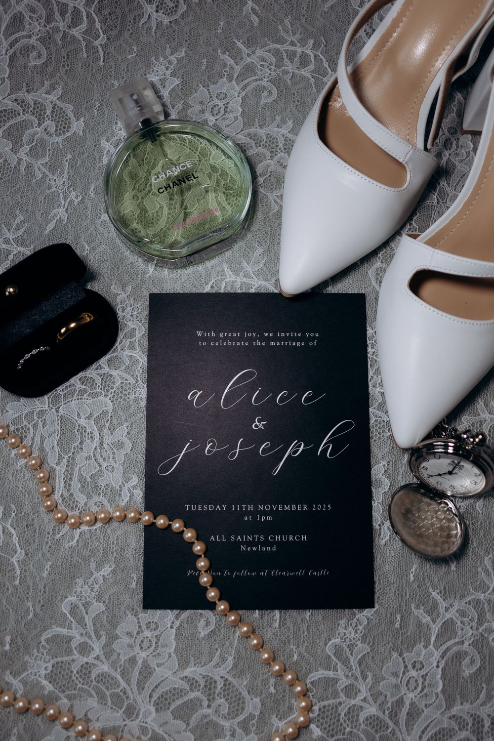 Wedding invitation with white shoes, perfume bottle, and pearl necklace arranged on lace background.