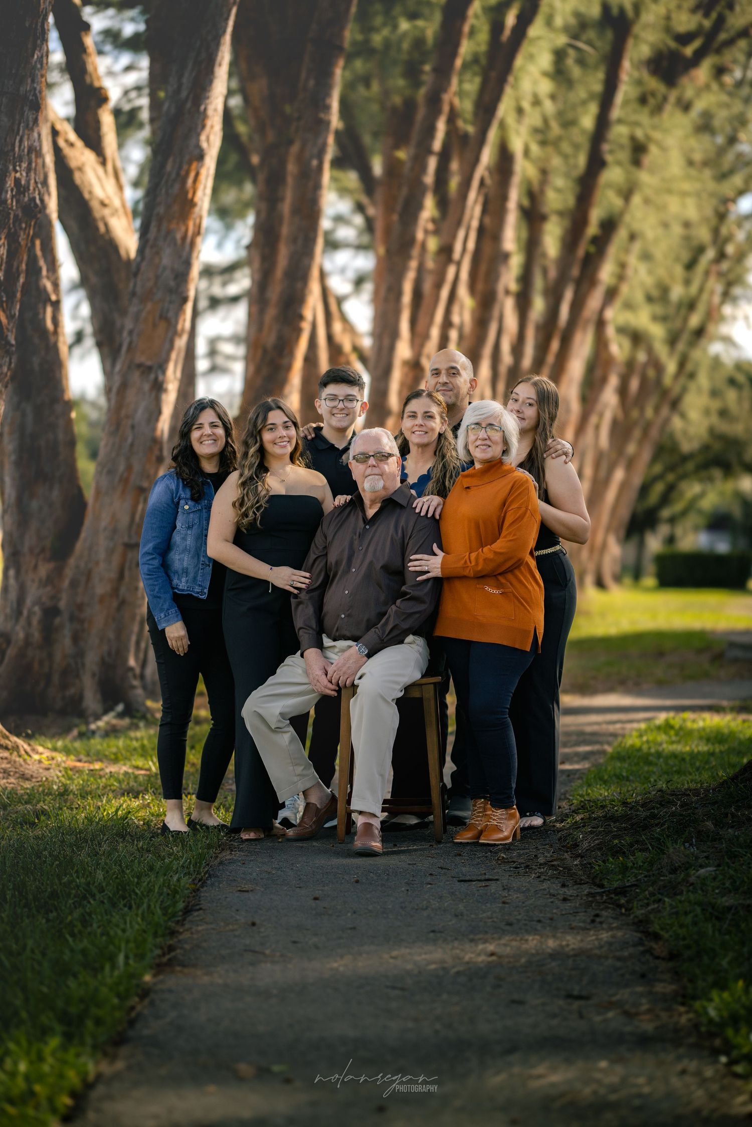Large family group portrait taken outdoors among tall pine trees during golden hour.
