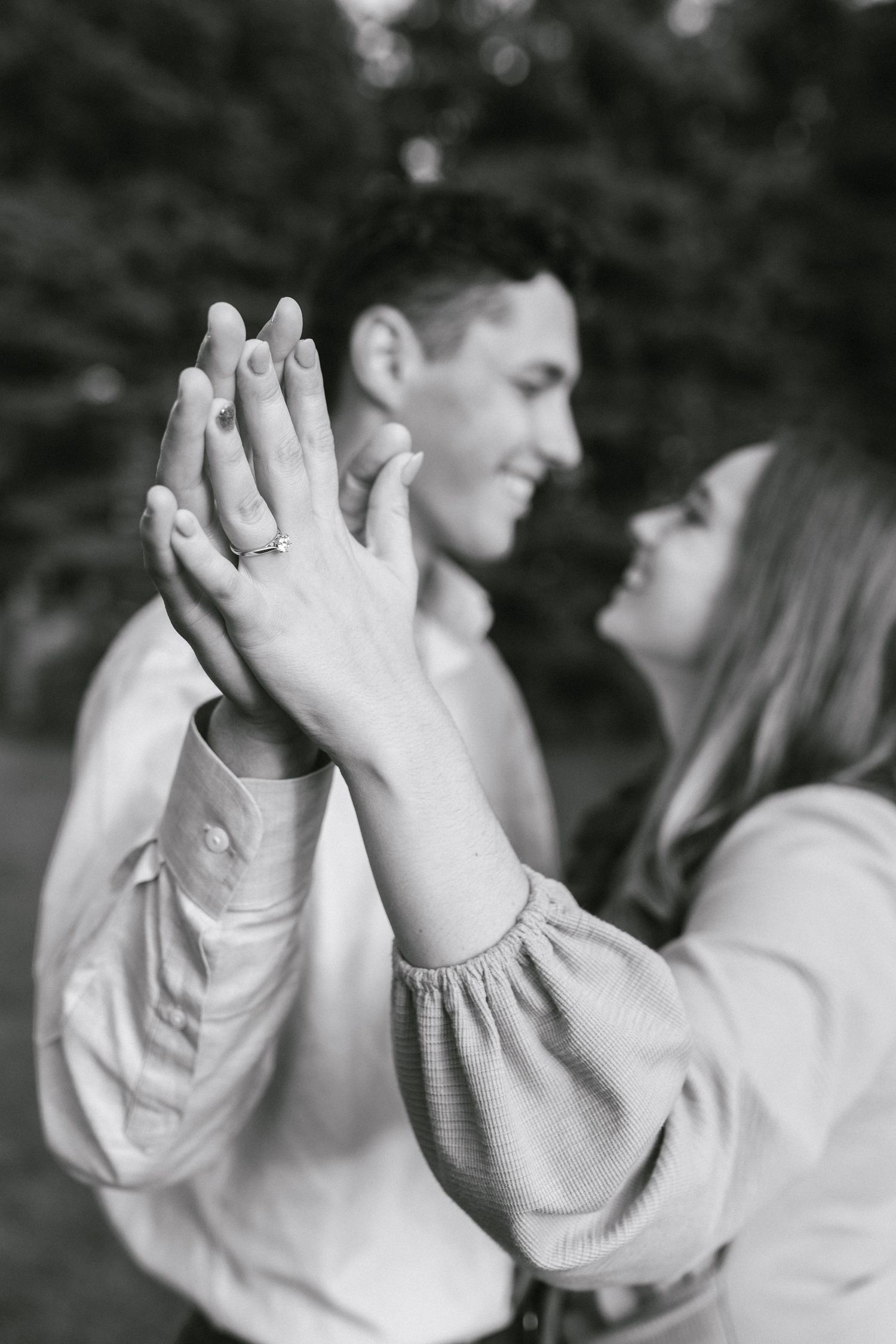 Black and white photo of couple holding hands while gazing at each other outdoors.