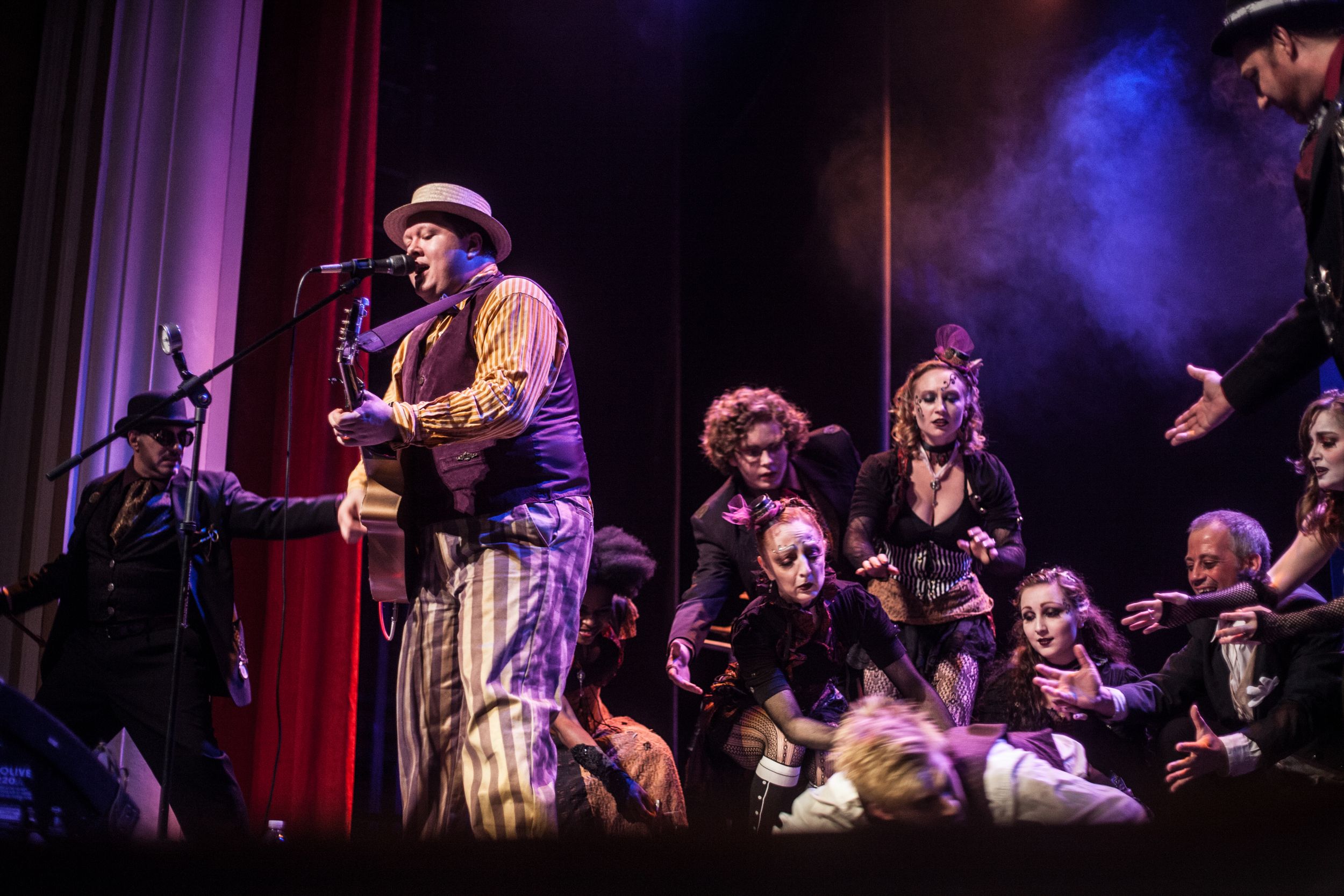 Musicians performing on stage with chorus members in background.