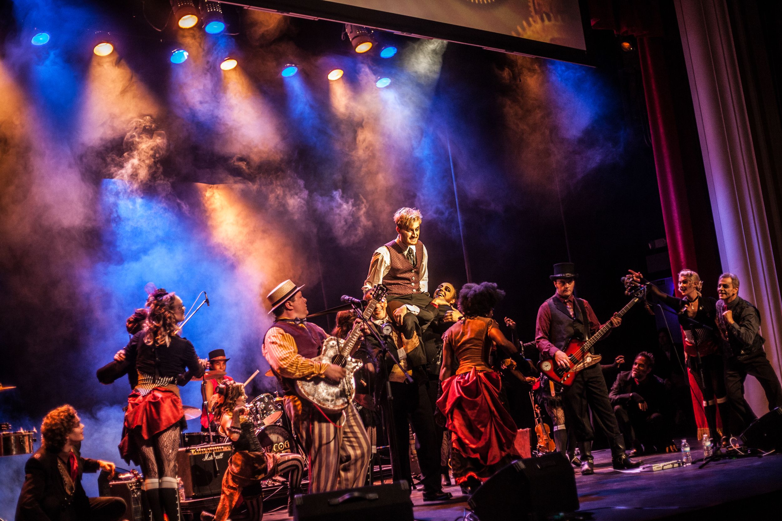 Large ensemble performs theatrical steampunk show with dramatic lighting and stage effects.