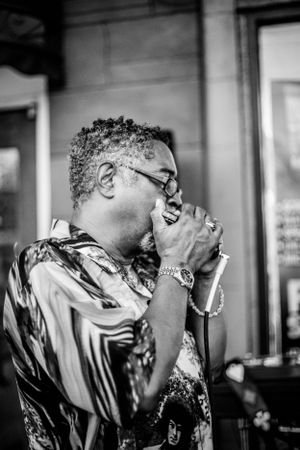 Musician plays harmonica in black and white portrait with dramatic side lighting.
