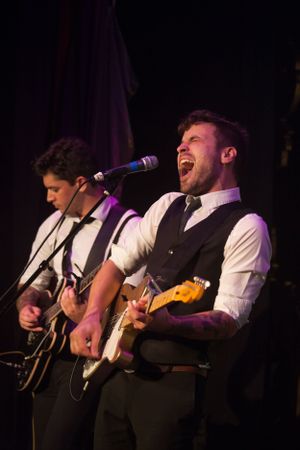 Musicians in vests perform passionately on electric guitar during a concert performance.