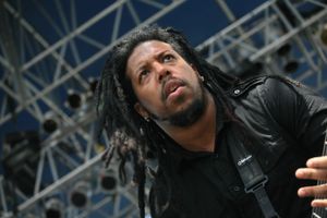 Performer with dreadlocks in black clothing singing on stage during a concert performance.