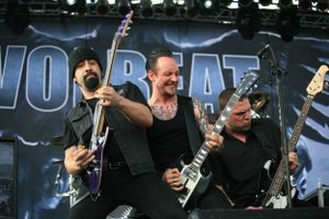 Three musicians performing together on guitars during heavy metal concert on outdoor stage.