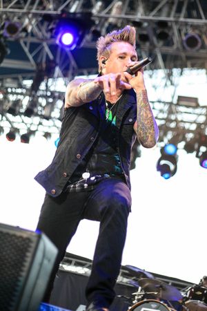Performer with spiked hair sings into microphone during outdoor concert performance.