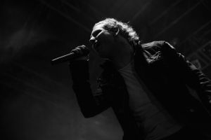 Dramatic black and white photo of performer singing on stage in dark lighting.