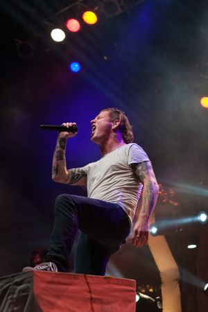Rock performer in white t-shirt singing passionately under colorful stage lights.