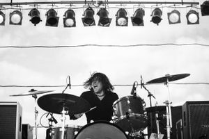 Black and white photo of drummer performing intensely behind drum kit under stage lights.