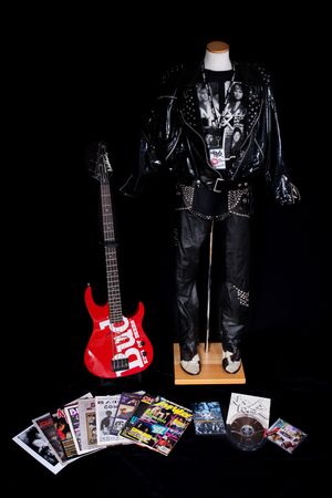 Display of rock music memorabilia with red guitar, leather outfit, and album collection on black background.