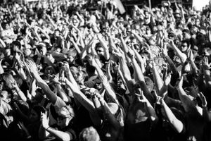 Black and white crowd photo showing sea of raised arms at outdoor concert venue.