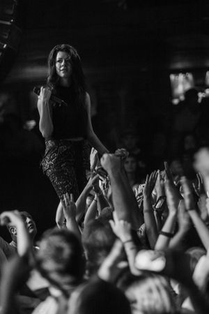 Concert performer stands above crowd of raised hands in dramatic black and white photo.