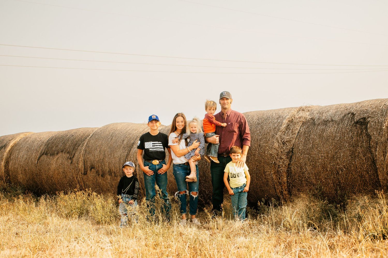 Family posed together against large hay bales in rural field setting.