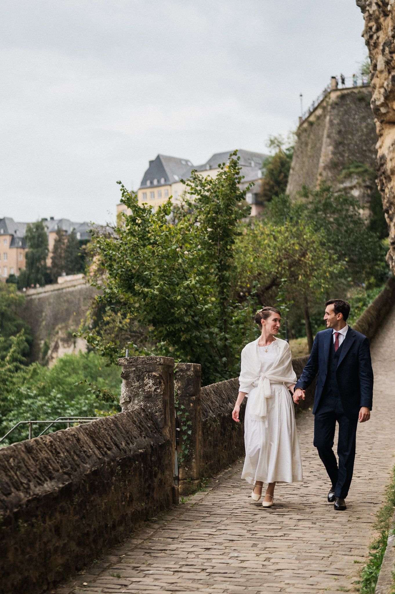 A couple strolls along a cobblestone path beside ancient stone walls in Luxembourg's historic old town.