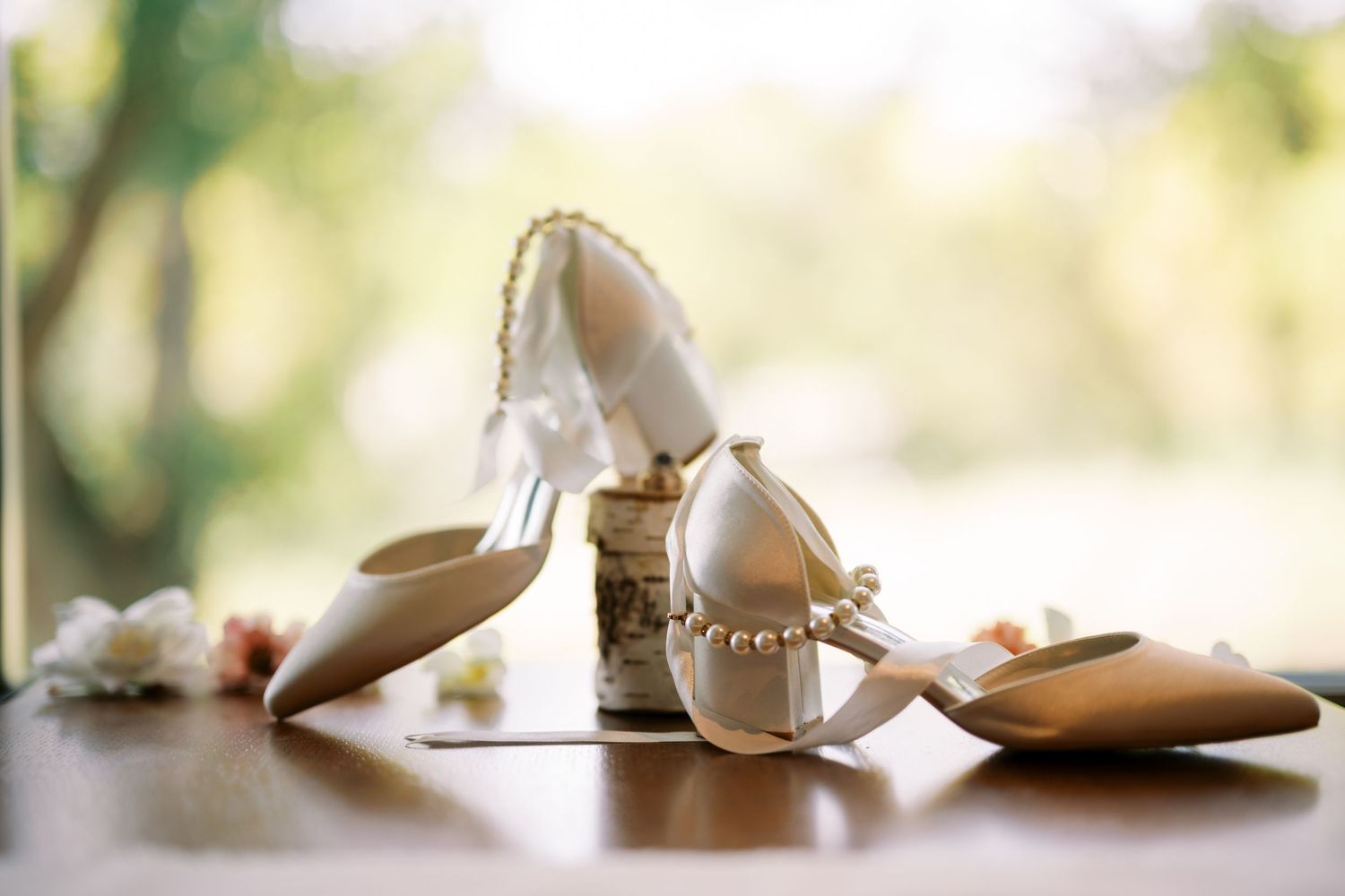 Elegant bridal shoes and flats with pearls and embellishments arranged on reflective surface in soft natural light.