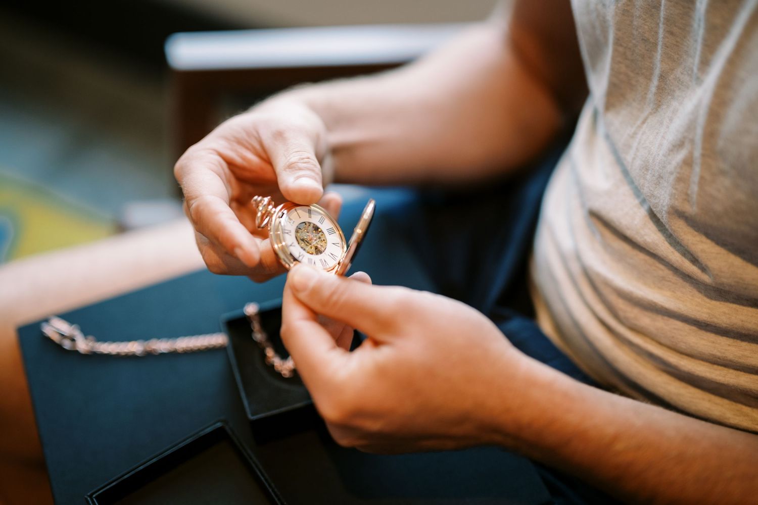 Close-up view of hands holding and examining a piece of jewelry or timepiece in soft lighting.