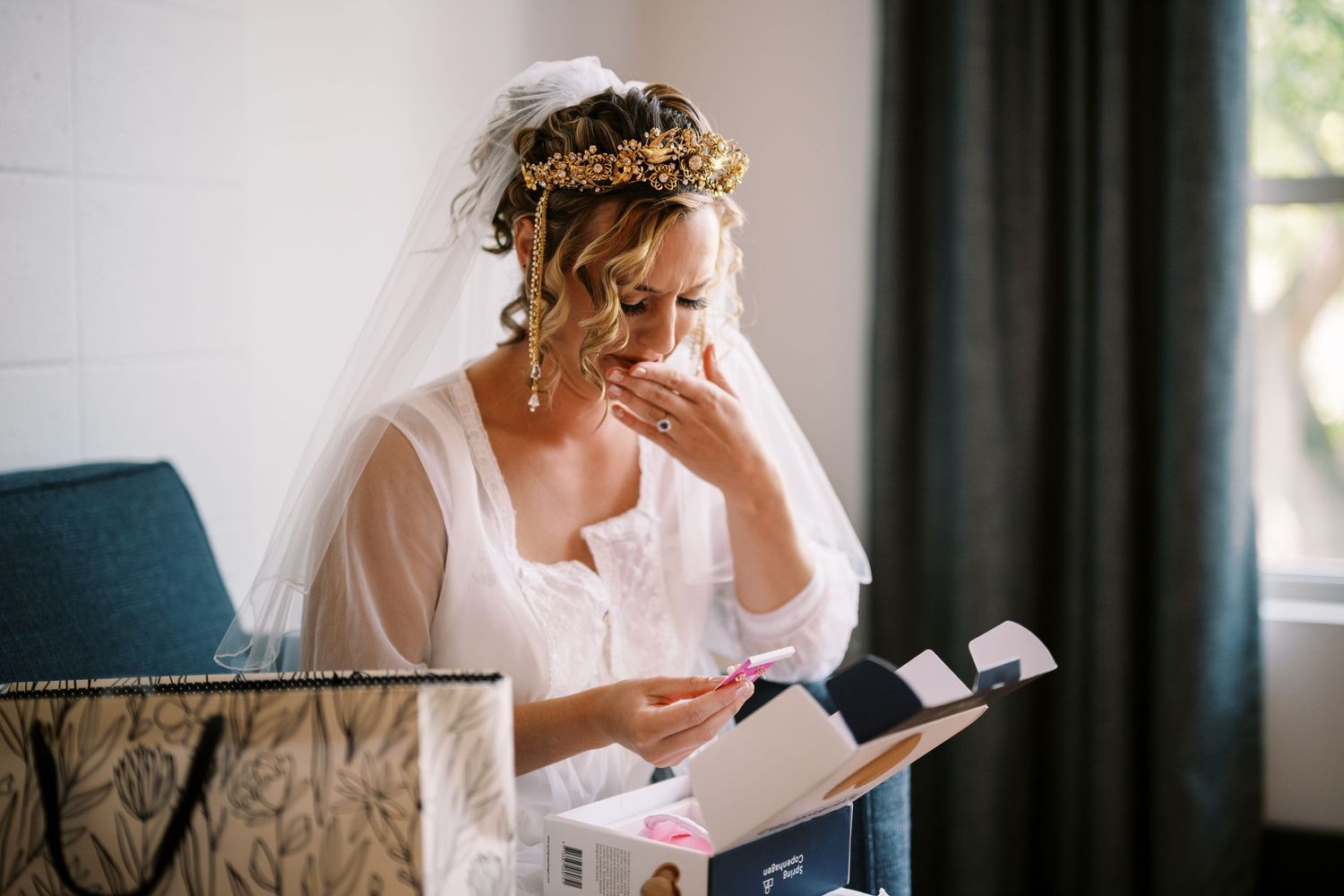 A bride in a white robe and veil reads a letter while getting ready on her wedding day.
