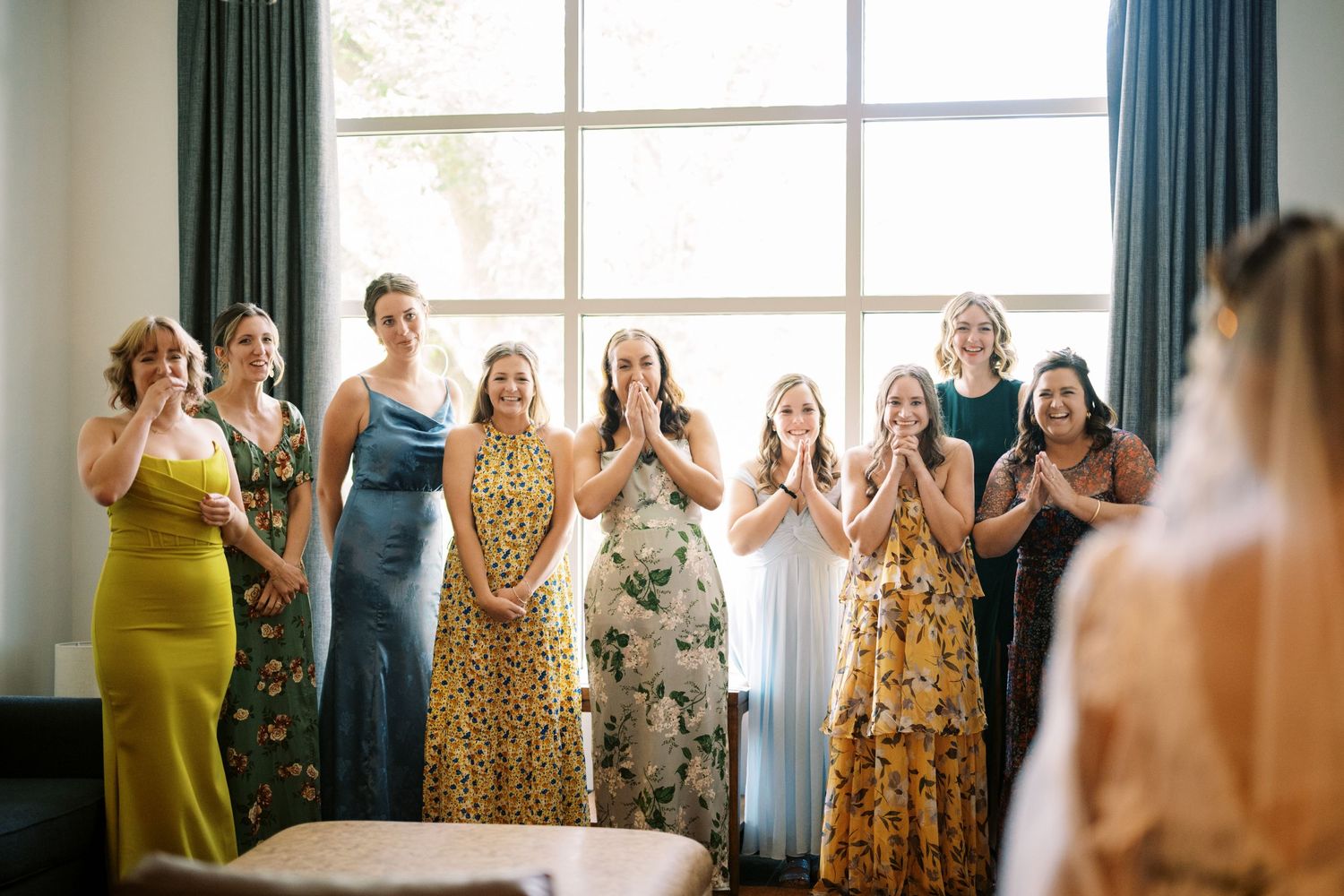 Wedding guests in colorful dresses react emotionally during an intimate indoor celebration moment.