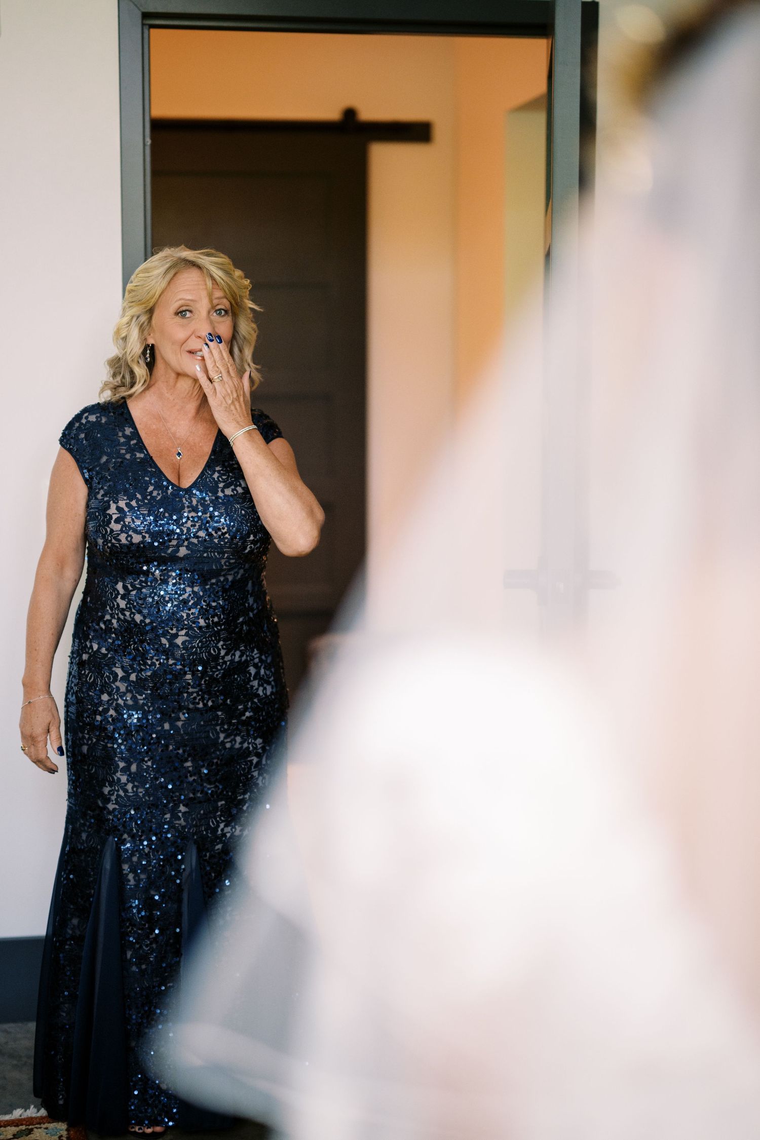 Woman in navy blue sequined evening gown shows emotional reaction while standing in doorway.