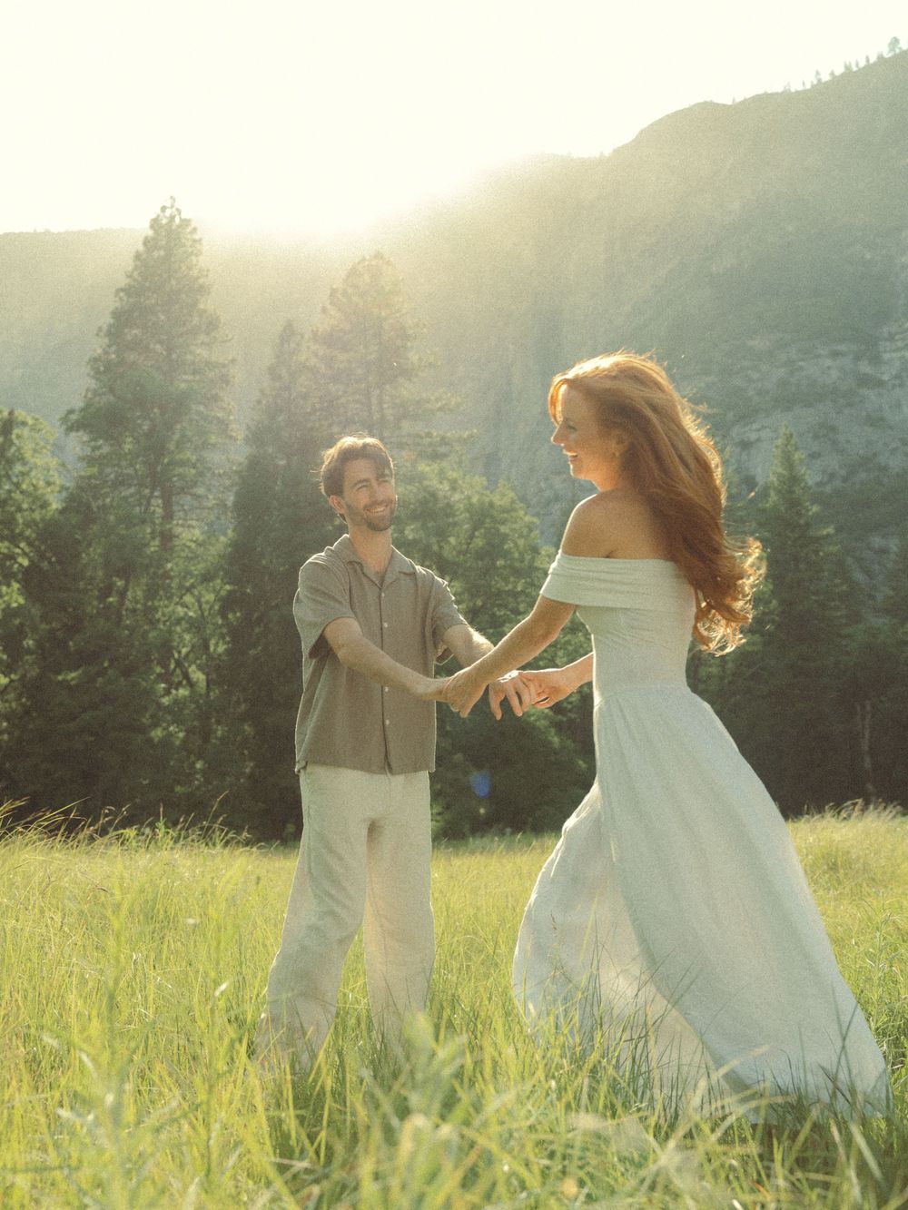 A couple dancing together in a sunlit meadow against a mountainous backdrop during golden hour.