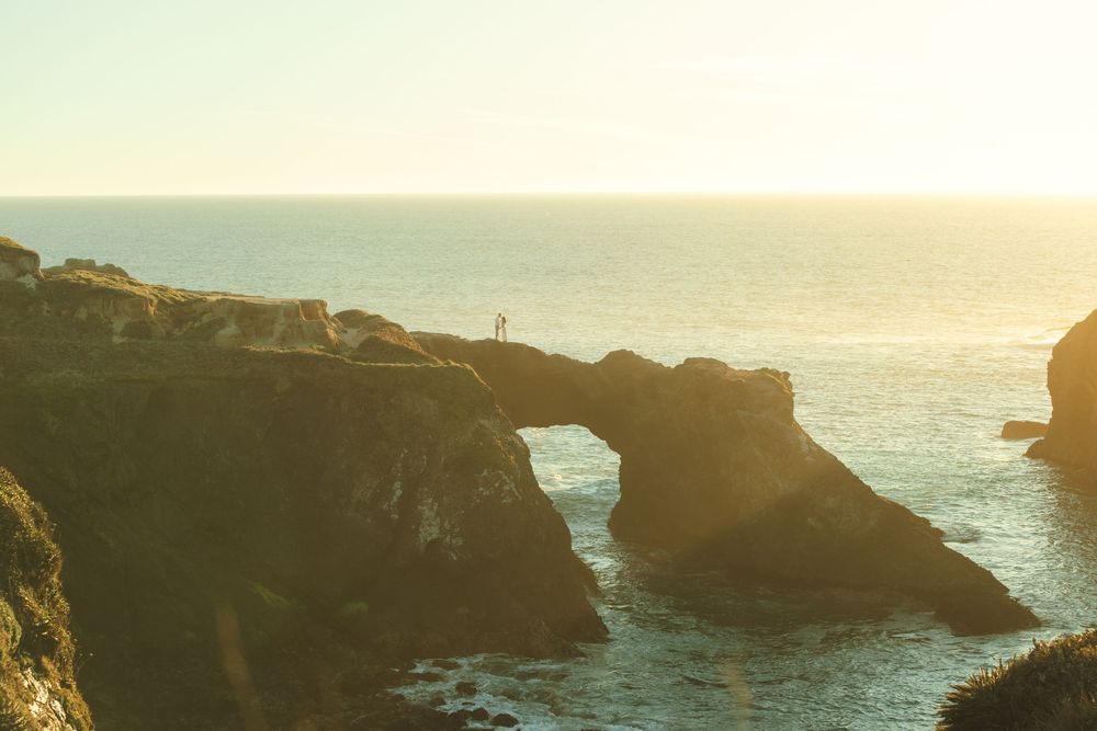 Natural stone arch formation along a rocky coastline at sunset with golden light reflecting off the ocean waves.