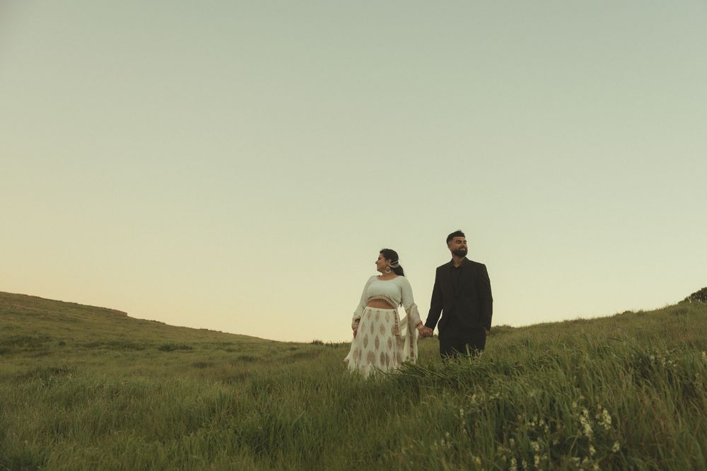 Two figures stand together on a grassy hillside against a soft sunset sky.