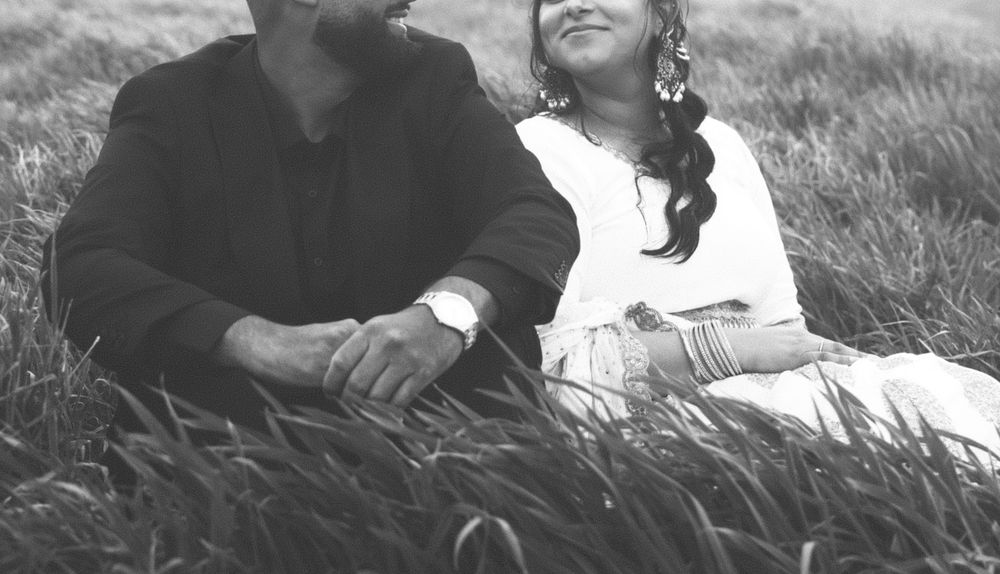 A black and white photo shows a group of people sitting together in tall grass on a hillside.