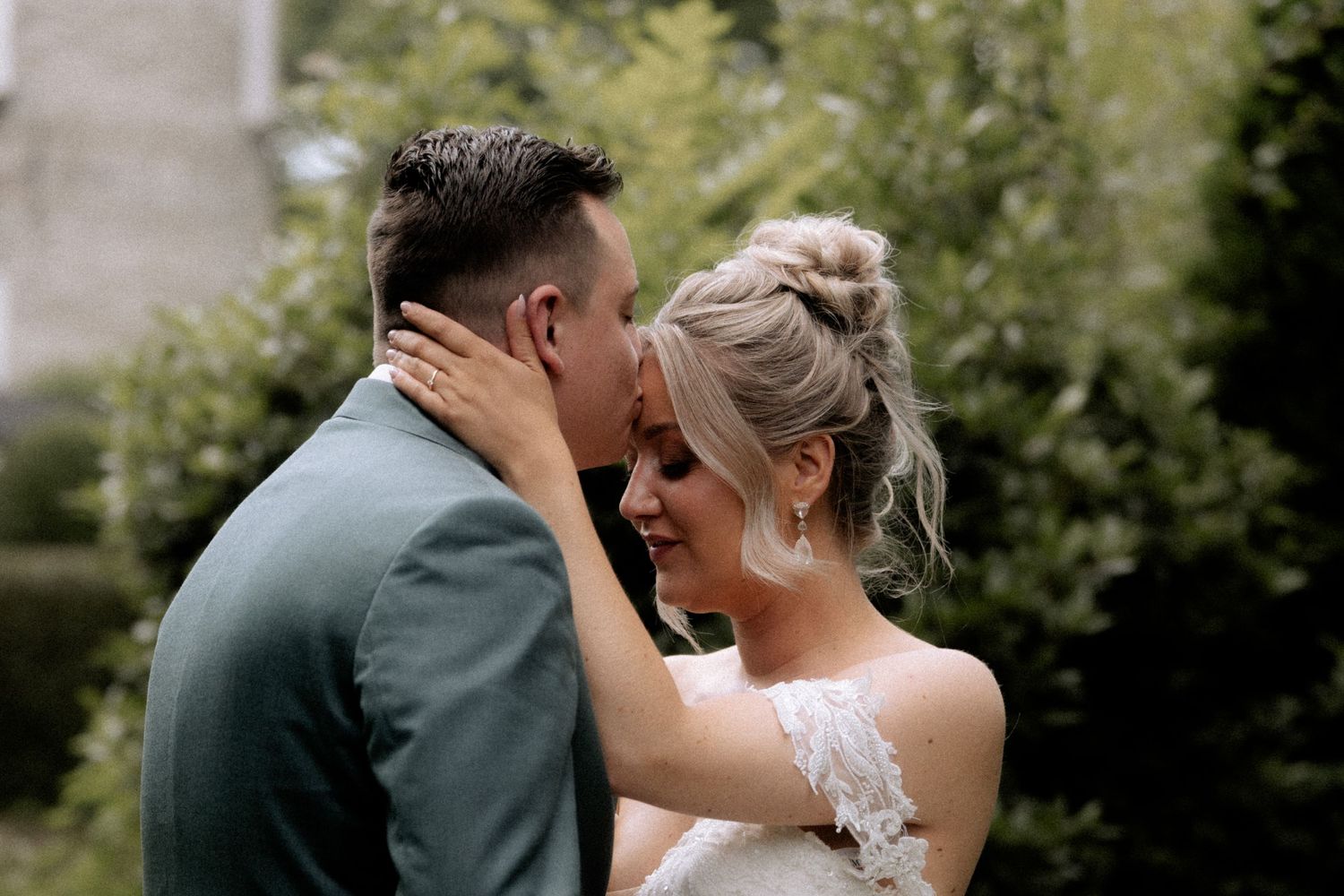 A tender moment between a couple on their wedding day with green foliage in the background.