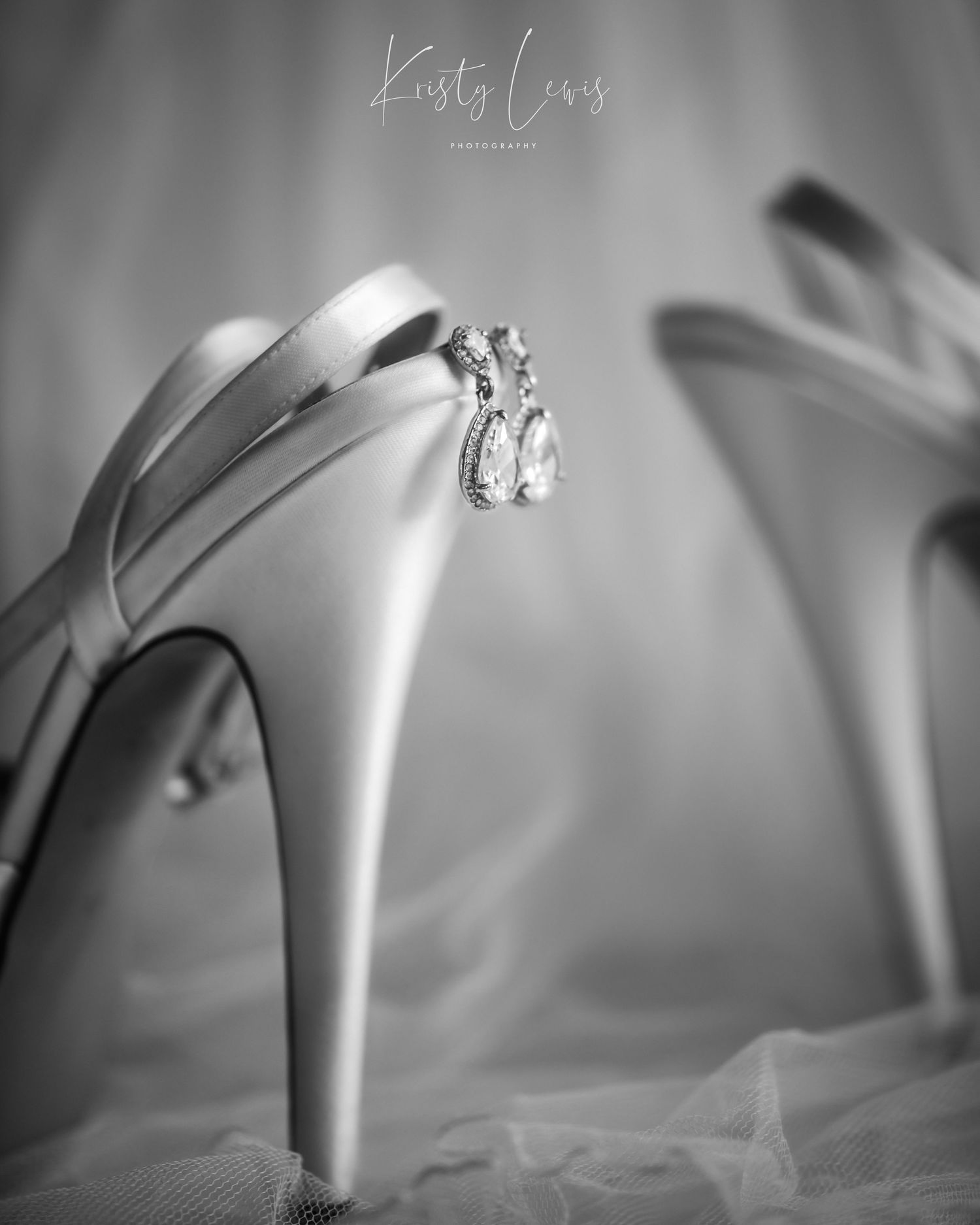 Detailed black and white image of white satin bridal shoes with diamond earrings hanging off the back of the shoe. Shot in Blackwood, Wales