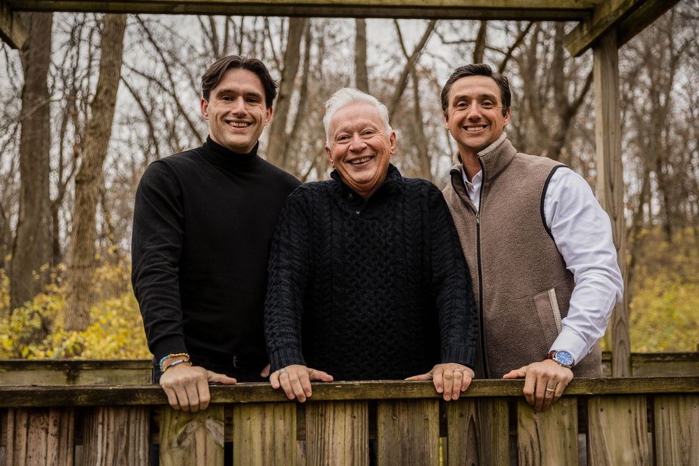 A group of people pose together in an outdoor setting with autumn trees in the background.