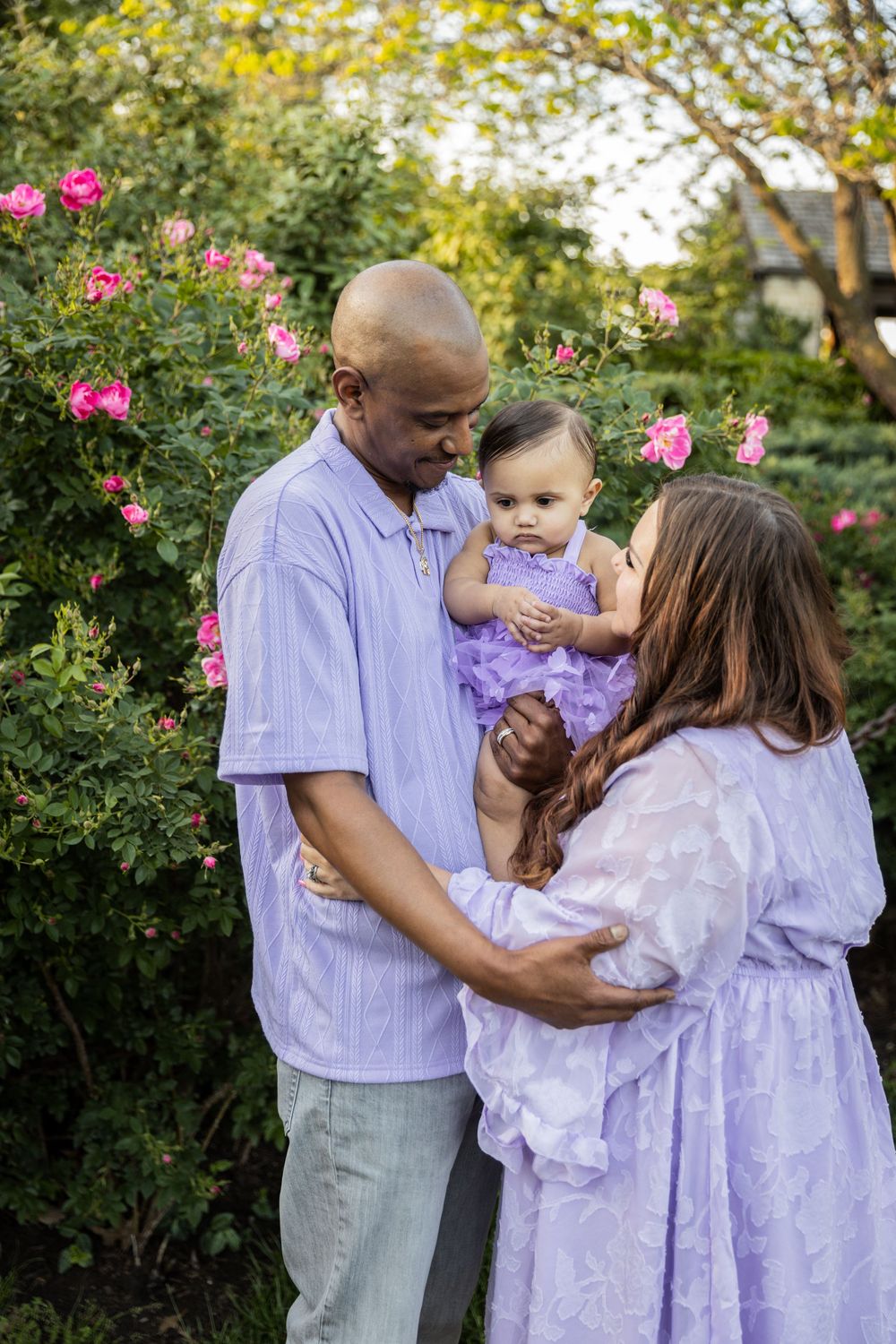 Family in coordinating purple outfits poses together in garden with pink flowers.