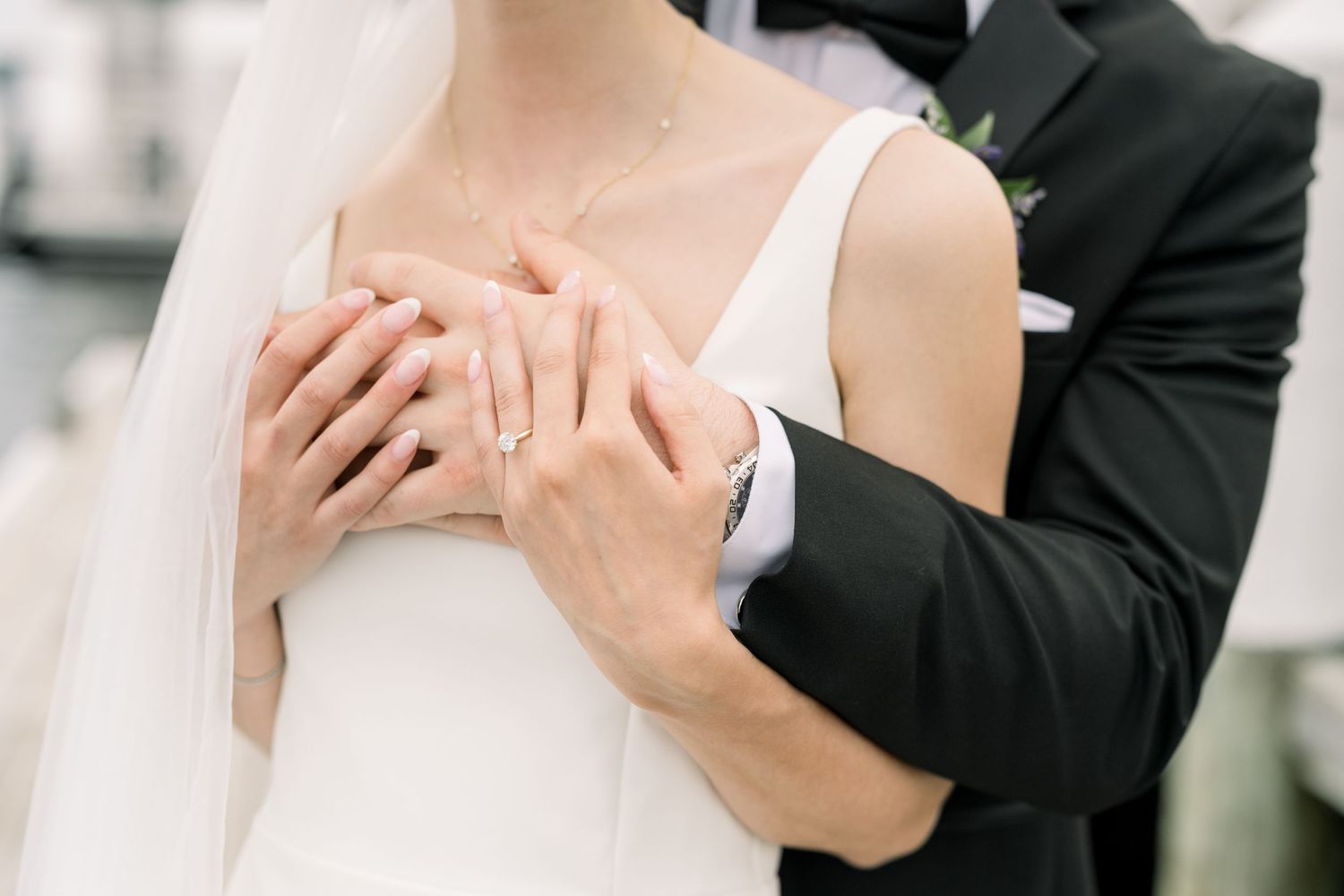 An intimate wedding moment showing hands embracing, with a bride in white dress and groom in black suit.