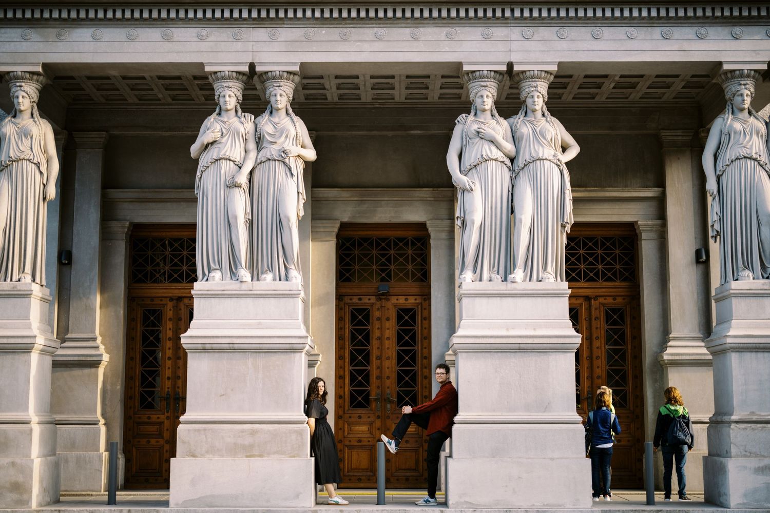 Classical stone caryatid columns frame ornate wooden doors at the entrance of a grand historic building.