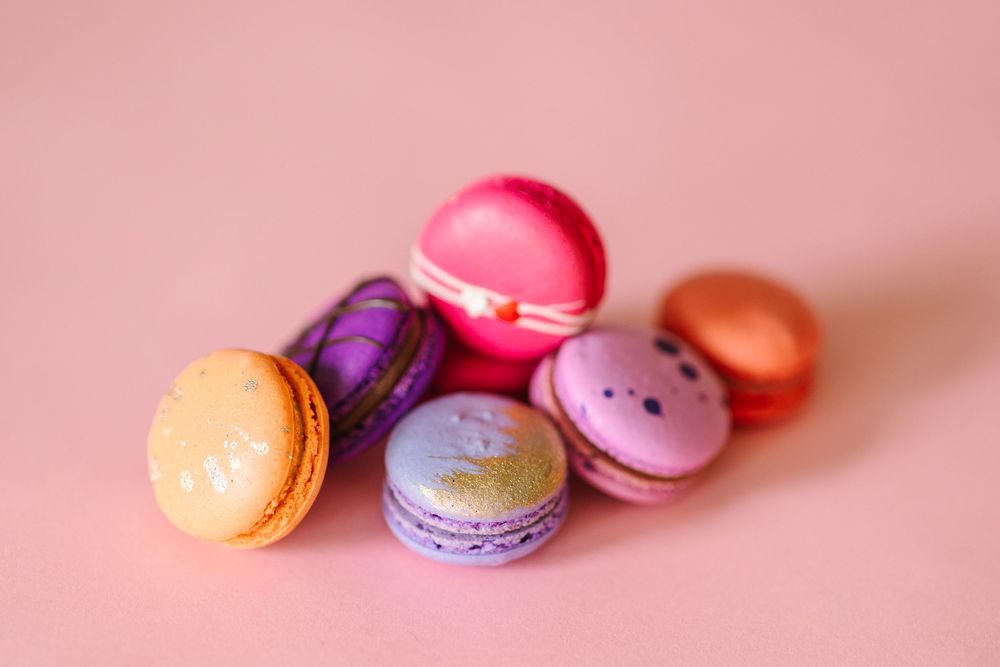 Colorful French macarons displayed on a pink background showing various pastel shades.