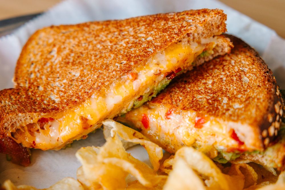 Grilled cheese sandwich with melted cheese and chips served on white paper.