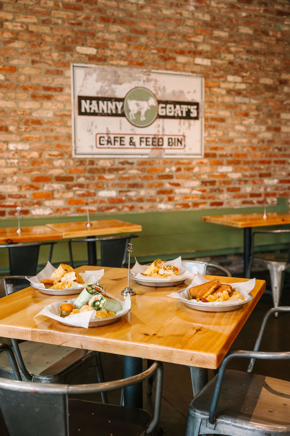 Rustic cafe interior with wooden tables and metal chairs against exposed brick wall.